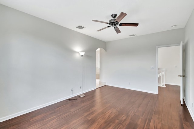 empty room featuring arched walkways, dark wood-type flooring, a ceiling fan, visible vents, and baseboards