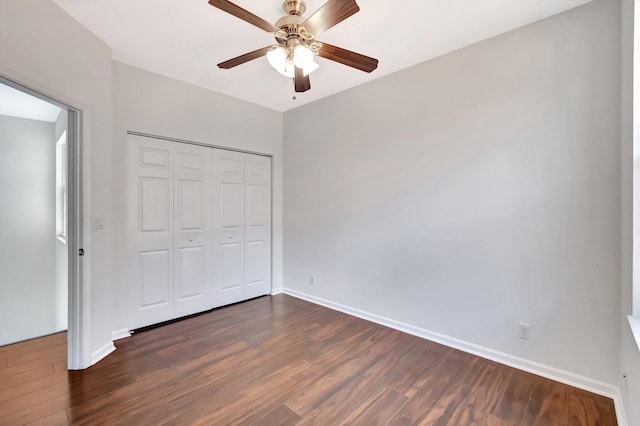 unfurnished bedroom featuring dark wood-type flooring, a closet, baseboards, and a ceiling fan