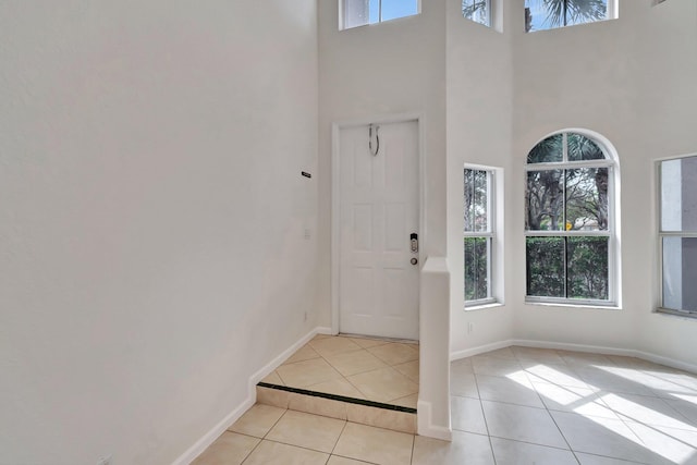 entrance foyer with a high ceiling, light tile patterned flooring, a wealth of natural light, and baseboards