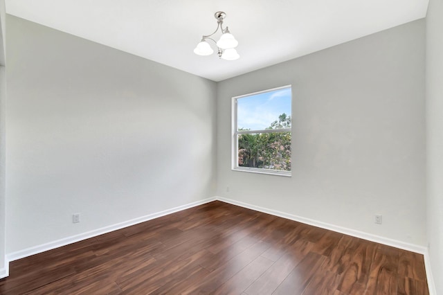 empty room featuring dark wood-style floors, a notable chandelier, and baseboards