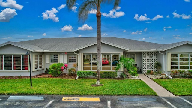 ranch-style house featuring stucco siding, a shingled roof, uncovered parking, and a front yard