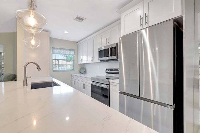 kitchen with light stone counters, stainless steel appliances, hanging light fixtures, white cabinetry, and a sink