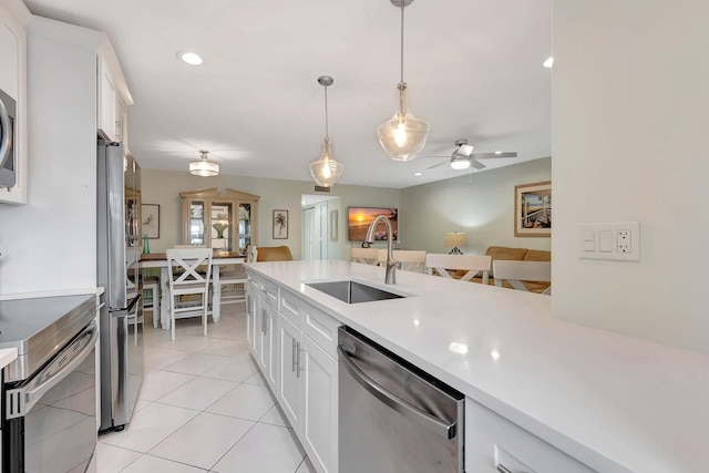 kitchen with decorative light fixtures, stainless steel appliances, light countertops, white cabinets, and a sink