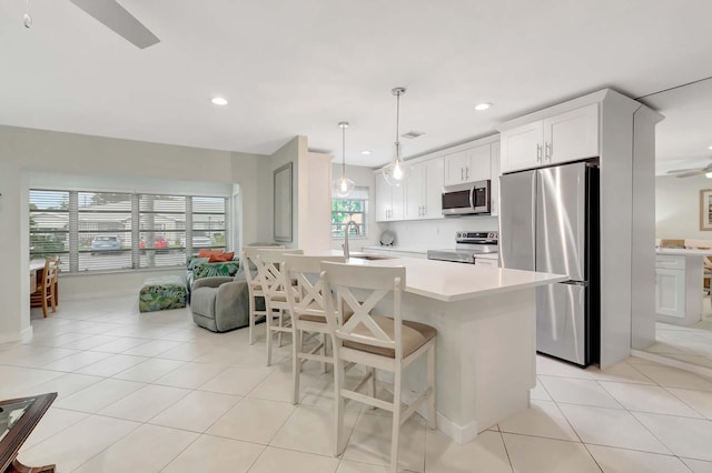 kitchen featuring stainless steel appliances, light countertops, white cabinets, a sink, and a kitchen bar