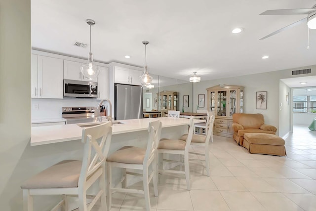 kitchen with decorative light fixtures, light countertops, appliances with stainless steel finishes, white cabinets, and a kitchen breakfast bar