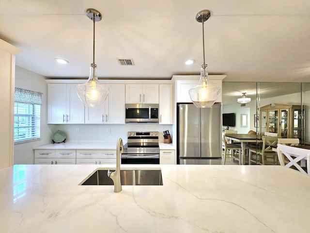 kitchen featuring visible vents, hanging light fixtures, appliances with stainless steel finishes, white cabinets, and a sink