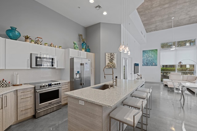 kitchen with a kitchen breakfast bar, a kitchen island with sink, stainless steel appliances, pendant lighting, and a sink