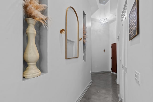 hall with concrete floors, baseboards, and a chandelier