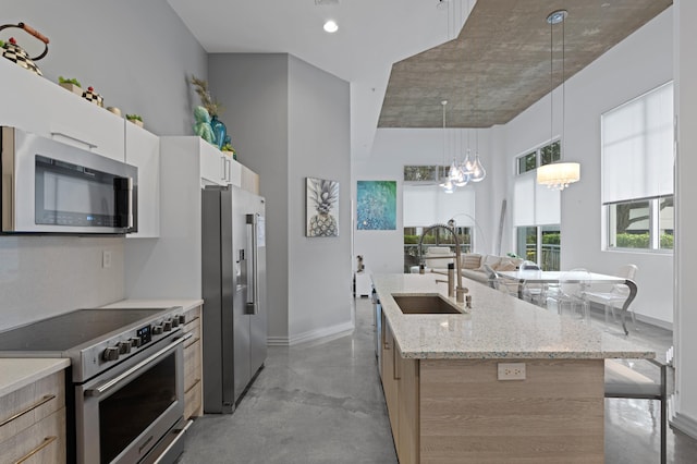 kitchen featuring concrete flooring, a sink, white cabinetry, appliances with stainless steel finishes, and a center island with sink