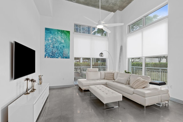 living room featuring a towering ceiling, ceiling fan, concrete floors, and baseboards