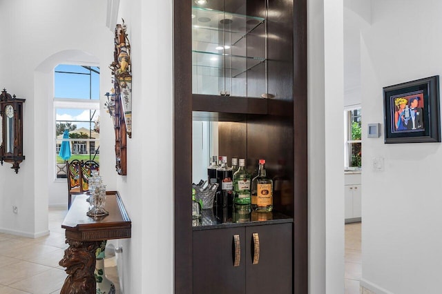 bar featuring a bar, baseboards, arched walkways, and light tile patterned flooring