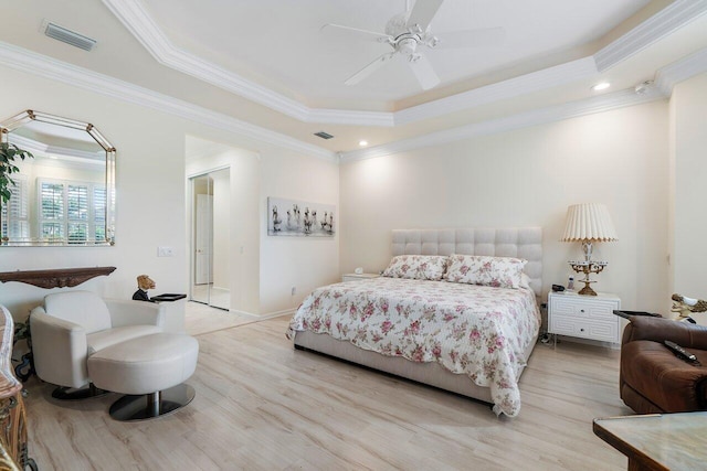 bedroom with light wood-style floors, a tray ceiling, visible vents, and ornamental molding