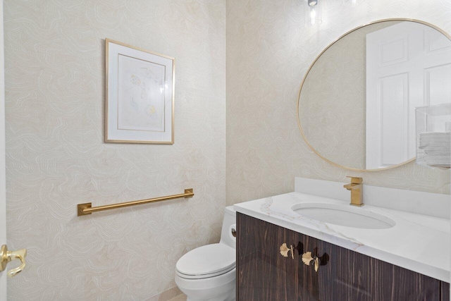 half bath featuring toilet, wallpapered walls, and vanity