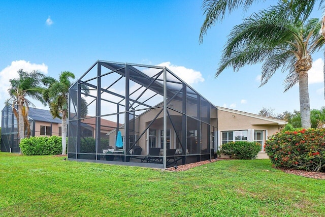 rear view of property featuring a lanai, a yard, and stucco siding