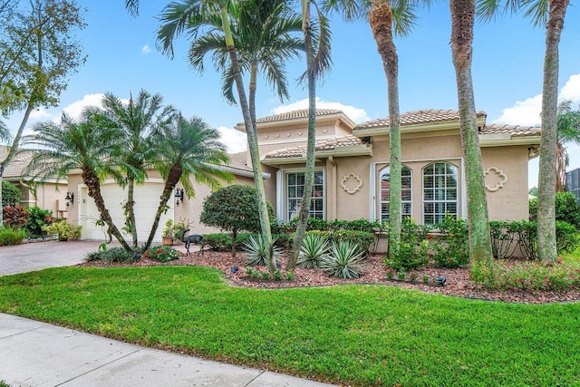 mediterranean / spanish home featuring stucco siding, a tile roof, decorative driveway, and a front yard