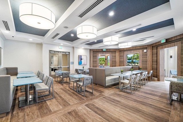 living room featuring a tray ceiling, visible vents, and wooden walls