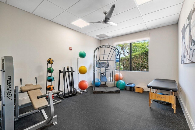 exercise area featuring a paneled ceiling, ceiling fan, and baseboards