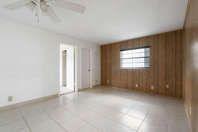 empty room with light tile patterned floors, wooden walls, baseboards, a ceiling fan, and a textured ceiling