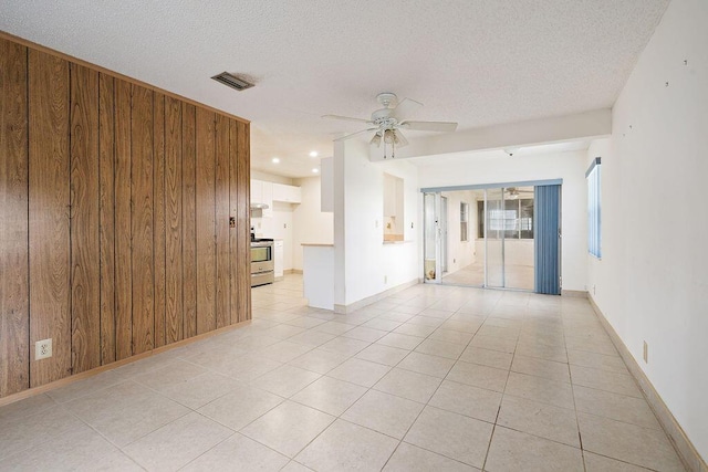 spare room with light tile patterned floors, visible vents, ceiling fan, wooden walls, and a textured ceiling