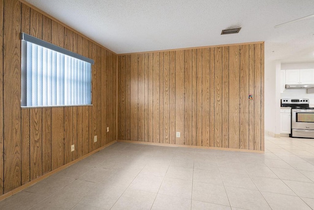 spare room with light tile patterned floors, baseboards, visible vents, a textured ceiling, and wood walls