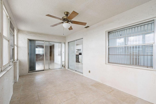 tiled empty room with ceiling fan, visible vents, a textured ceiling, and a textured wall