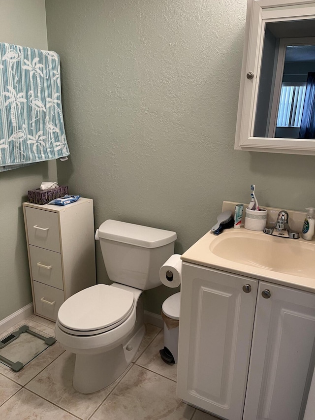 half bath featuring toilet, a textured wall, baseboards, and vanity