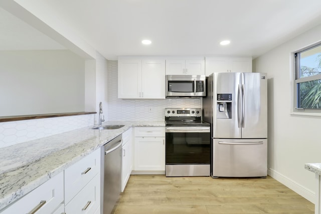 kitchen with white cabinets, light wood-style flooring, light stone counters, stainless steel appliances, and a sink