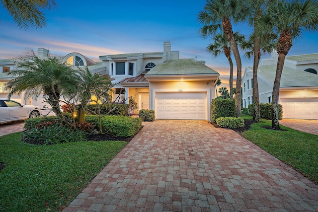 view of front of property featuring an attached garage, a chimney, decorative driveway, and stucco siding