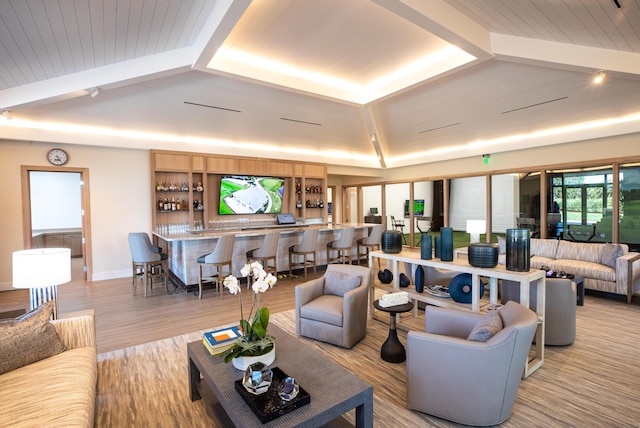 living room featuring light wood-style floors, a community bar, lofted ceiling with beams, and baseboards