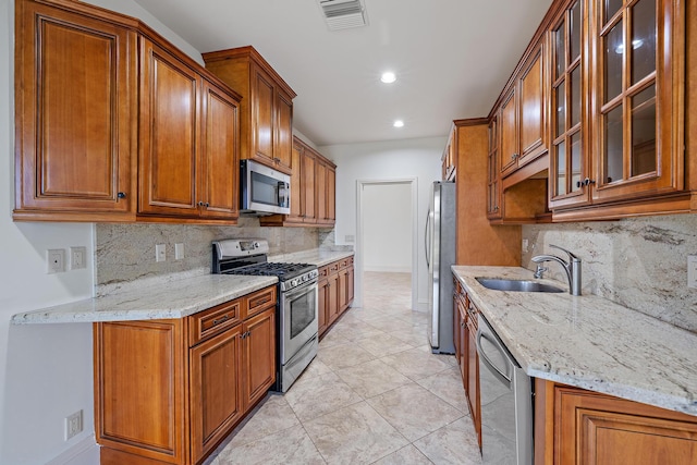 kitchen with stainless steel appliances, brown cabinets, visible vents, and light stone countertops