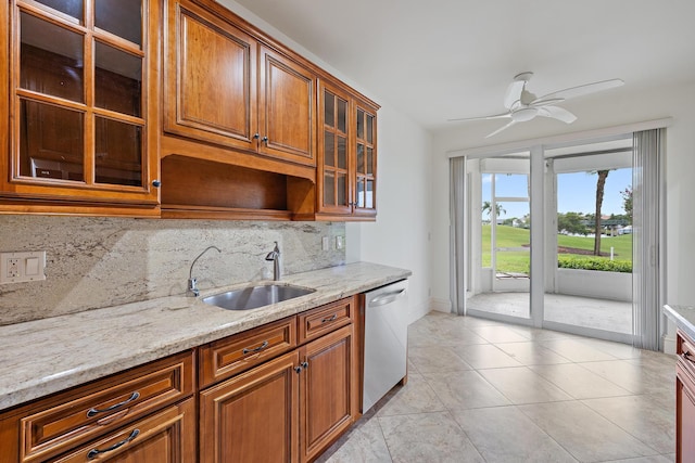 kitchen featuring glass insert cabinets, light stone counters, brown cabinets, a sink, and stainless steel dishwasher