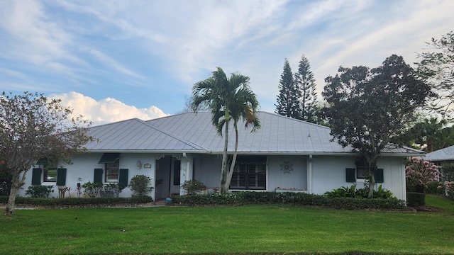 view of front facade with a standing seam roof, stucco siding, metal roof, and a front yard