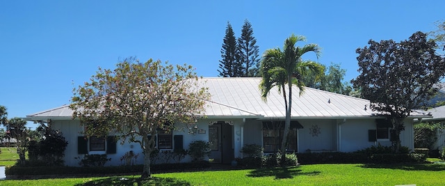 view of front of home with a standing seam roof, a front lawn, stucco siding, and metal roof