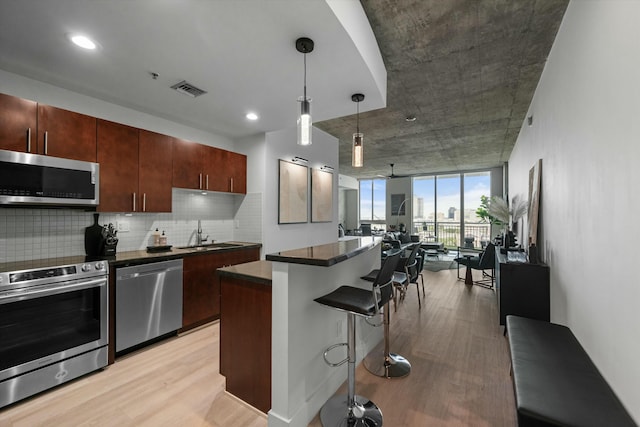 kitchen with a breakfast bar area, stainless steel appliances, dark countertops, decorative backsplash, and light wood-type flooring