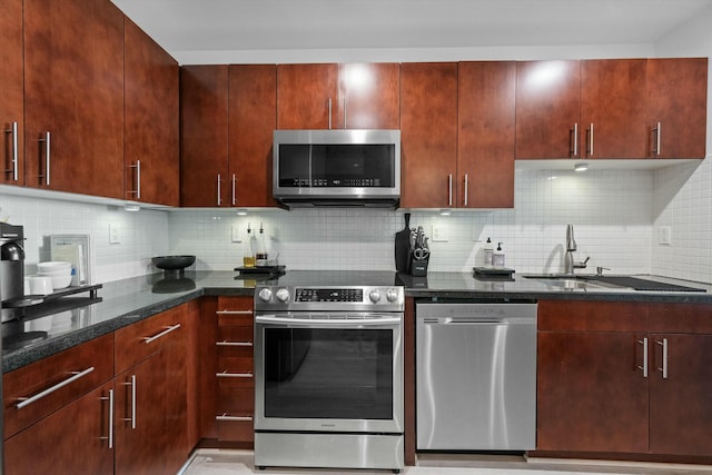 kitchen with appliances with stainless steel finishes, a sink, dark stone countertops, and tasteful backsplash