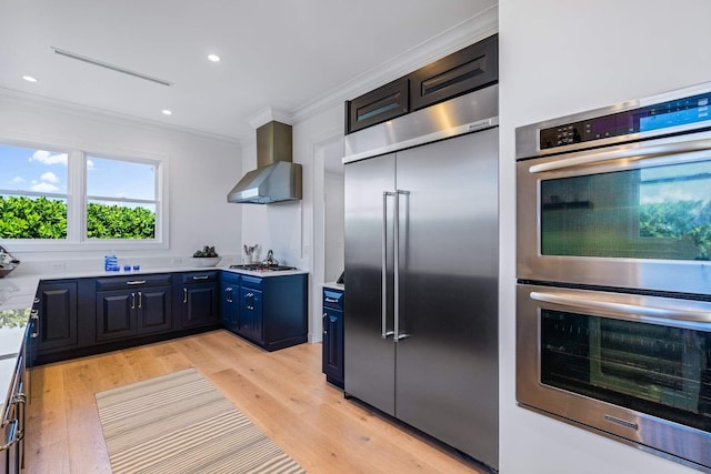 kitchen featuring stainless steel appliances, light wood-style floors, light countertops, ornamental molding, and wall chimney range hood