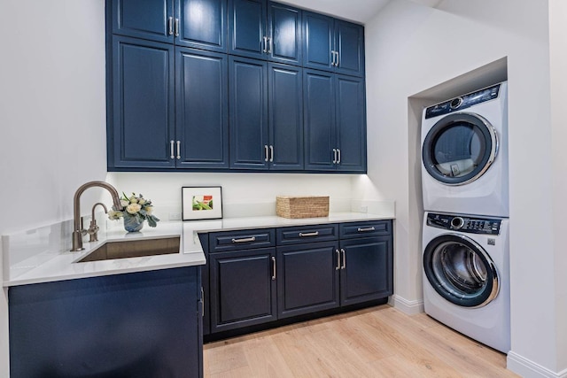 clothes washing area featuring a sink, baseboards, cabinet space, light wood finished floors, and stacked washer and clothes dryer