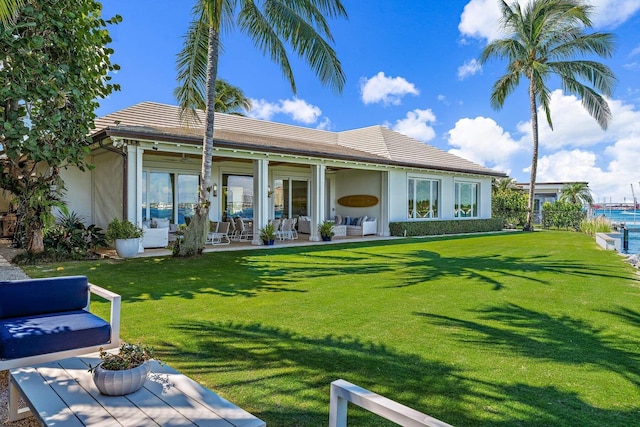 rear view of property featuring a lawn, a tiled roof, and stucco siding