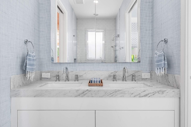 full bath featuring double vanity, a sink, tile walls, and a shower stall