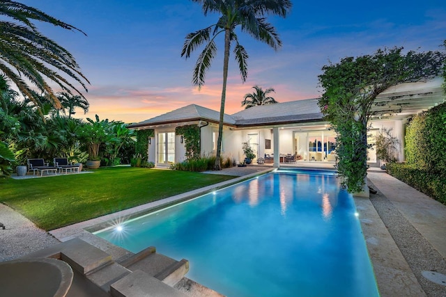 pool at dusk with a yard, an outdoor pool, and a patio