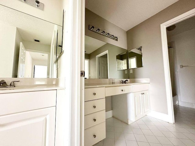 bathroom with a textured ceiling, a sink, two vanities, baseboards, and tile patterned floors