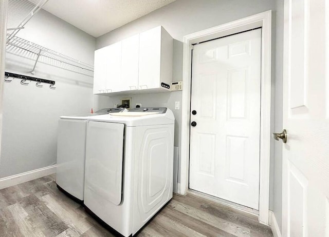 clothes washing area featuring baseboards, cabinet space, light wood-style flooring, and washing machine and clothes dryer