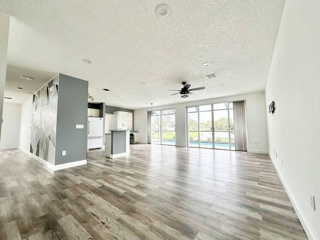 unfurnished living room with ceiling fan, a textured ceiling, wood finished floors, visible vents, and baseboards