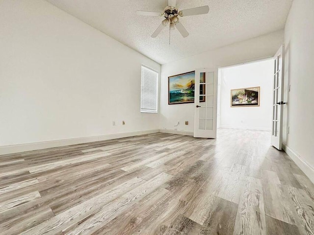 spare room with a textured ceiling, a ceiling fan, baseboards, light wood-style floors, and french doors