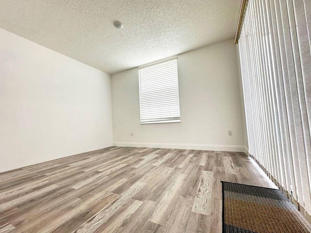 spare room featuring a textured ceiling, baseboards, and light wood-style floors