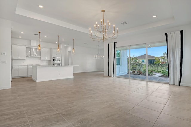 unfurnished living room with a tray ceiling, a notable chandelier, recessed lighting, visible vents, and baseboards