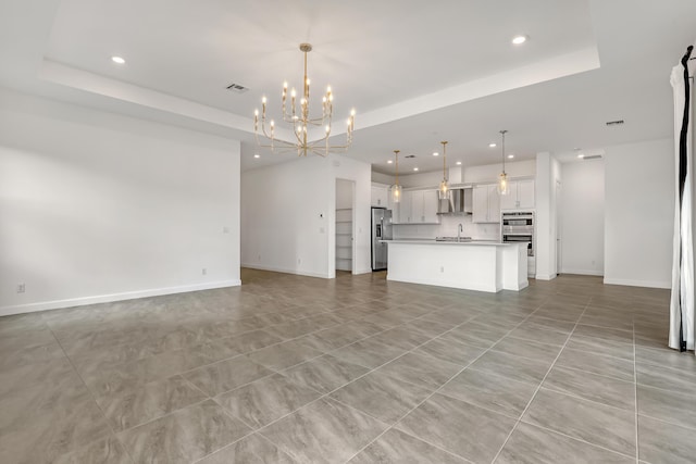 unfurnished living room featuring baseboards, a chandelier, a raised ceiling, and recessed lighting