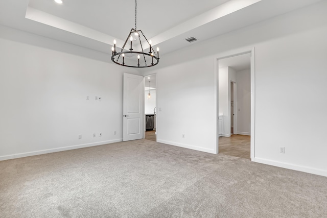 carpeted spare room featuring visible vents, a tray ceiling, and baseboards