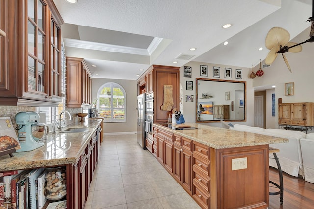 kitchen with a kitchen bar, glass insert cabinets, brown cabinetry, and a sink