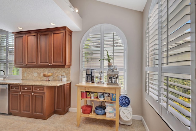 kitchen featuring dishwasher, light stone counters, backsplash, and baseboards